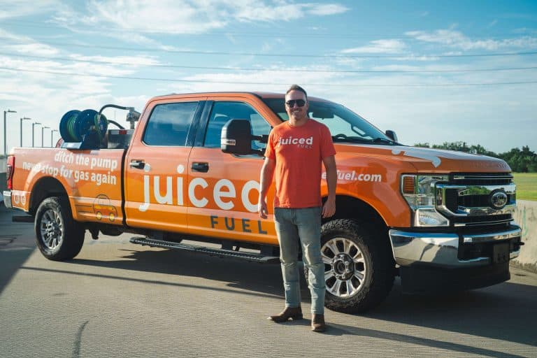 Korey McDavid standing in front of a Juiced Fuel delivery truck on a sunny day, wearing a branded orange t-shirt and sunglasses.