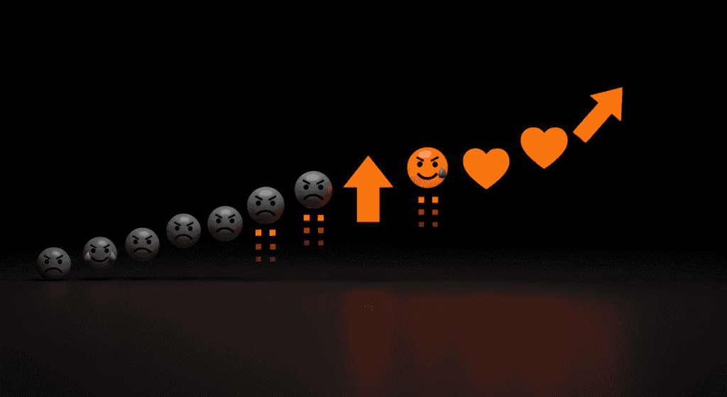 Digital concept art showing gray negative emojis transforming into bright orange hearts and arrows on a black background, symbolizing engagement and growth.
